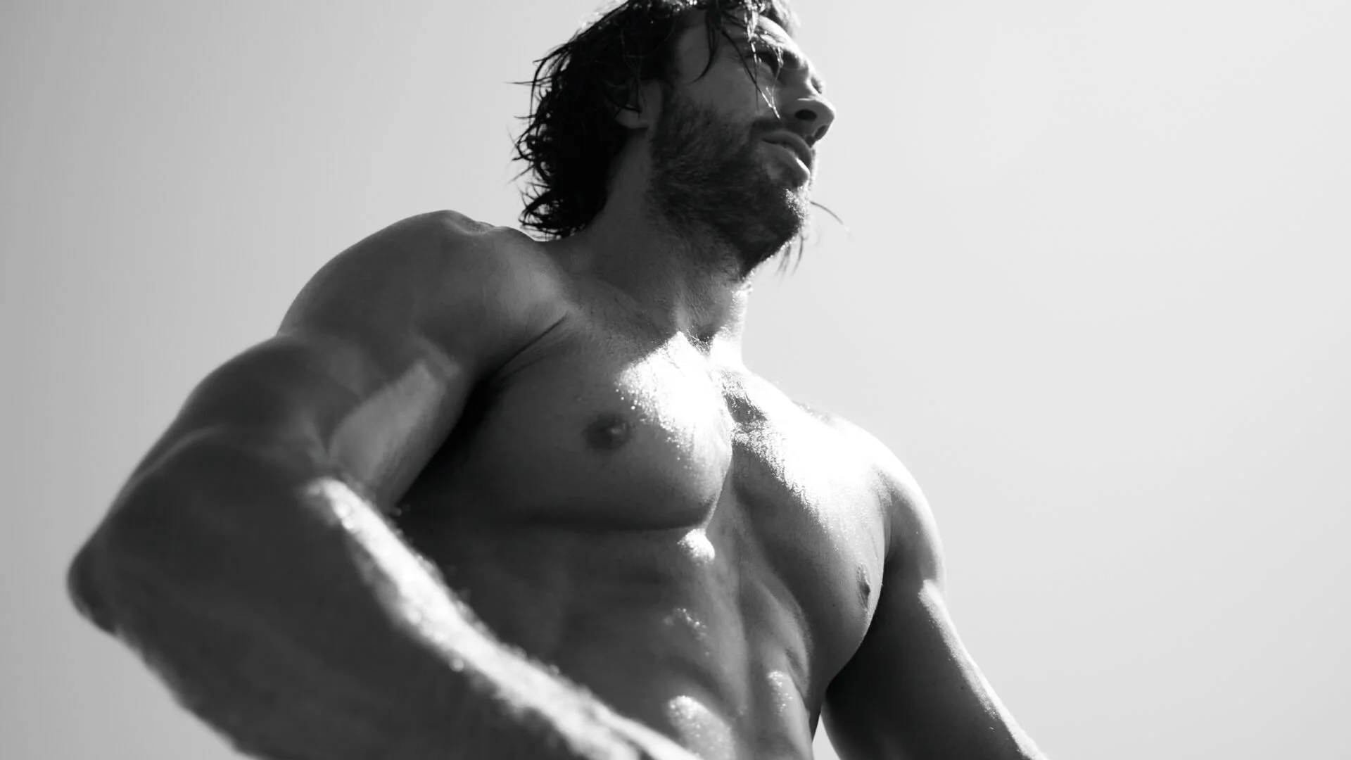 Homme torse nu avec des muscles bien définis, regardant vers le bas, en noir et blanc contre un fond clair.