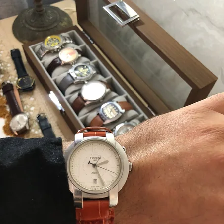 ⌚ montre au poignet est une Tissot Alarm Date (réf. T60.1.416.32 / L871/971) dotée d'un boîtier en acier inoxydable, d'un cadran blanc et d'un bracelet en cuir brun.