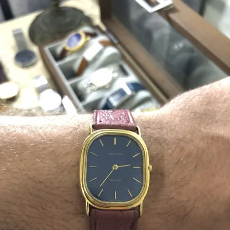 ⌚montre vintage Zenith quartz au boîtier ovale doré est dotée d'un élégant cadran bleu nuit et d'un bracelet en cuir grenu bordeaux.