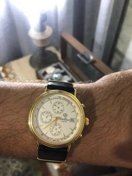 vintage Dom Baiz International Chronograph Watch featuring a classic white dial, three sub-dials, a date window at the 3 o'clock position, and a polished gold-plated case.