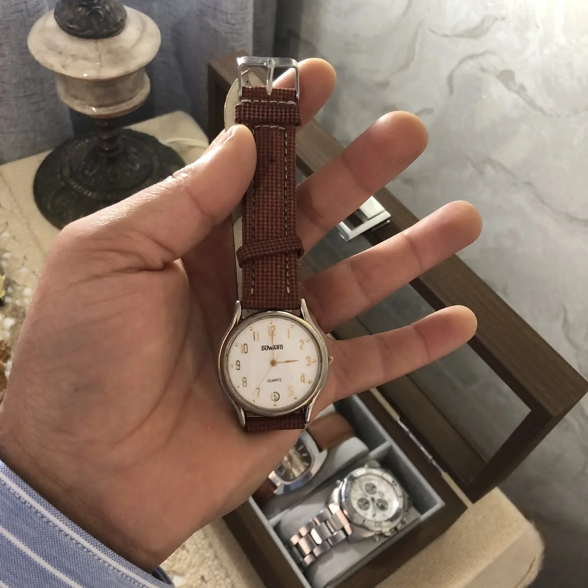 ⌚ Duward à mouvement quartz, dotée d'un cadran blanc avec des chiffres arabes dorés et d'un bracelet en cuir marron texturé.