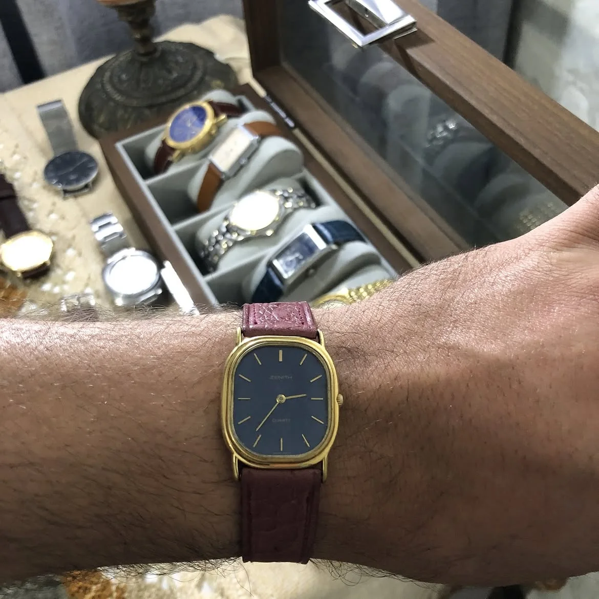 ⌚montre vintage Zenith quartz au boîtier ovale doré est dotée d'un élégant cadran bleu nuit et d'un bracelet en cuir grenu bordeaux.