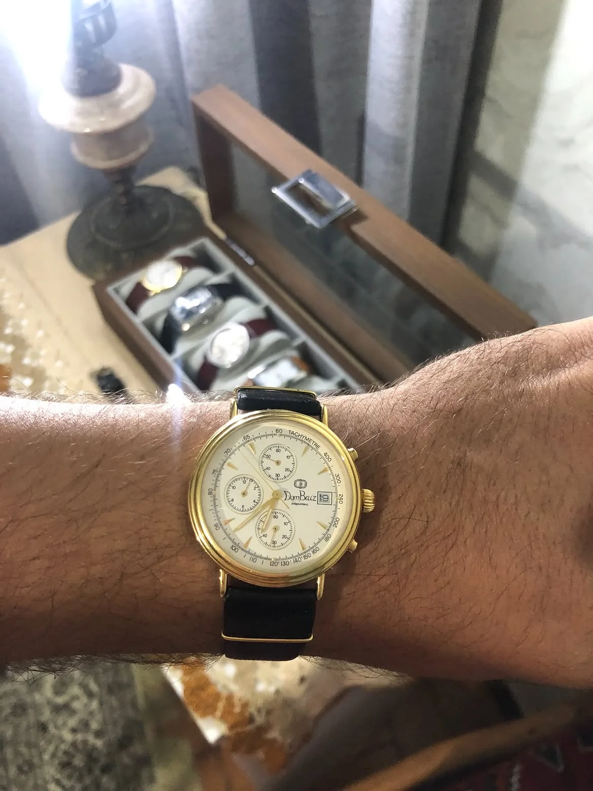 vintage Dom Baiz International Chronograph Watch featuring a classic white dial, three sub-dials, a date window at the 3 o'clock position, and a polished gold-plated case.