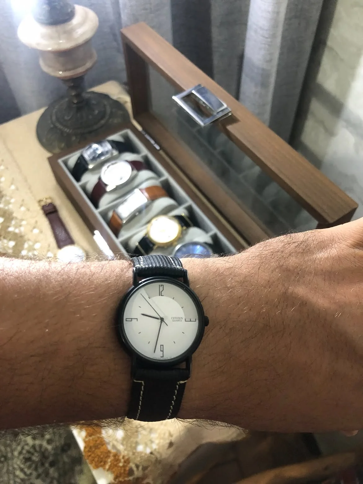 minimalist Citizen Quartz watch featuring a clean white dial, black matte case, and a textured black fabric or canvas strap.