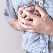 لقطة مقربة لصدر رجل يرتدي قميصا أزرق. يضع يده على قلبه ويبدو أنه يعاني من مشكلة في القلب والأوعية الدموية لأن يده متوترة.